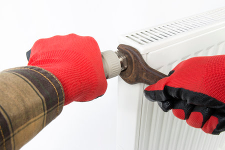 a technician tightens a central heating radiator fitting with a wrench, on isolated whiteの写真素材