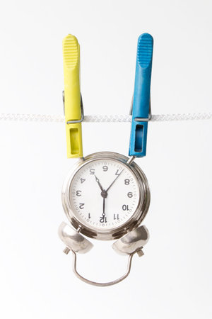 the alarm clock is fastened with a clothespins to a rope, dries on a rope, on a white isolated backgroundの写真素材