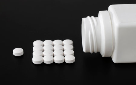 White pills spilled from a pill bottle on dark backgroundの写真素材