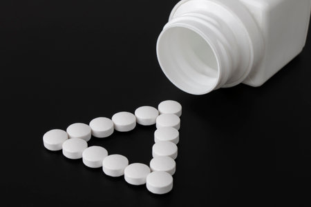 White pills stacked in a triangle next to a bottle of pills on a dark backgroundの写真素材