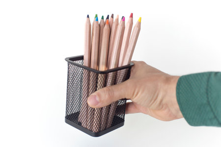 a hand holds a stationery glass with multi-colored pencils, on a white backgroundの写真素材