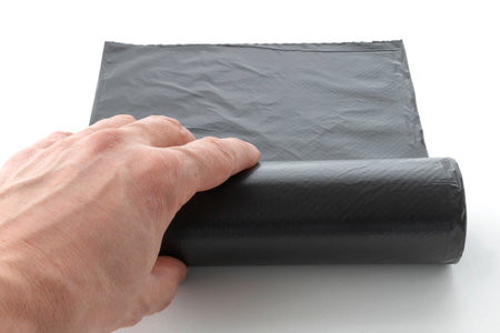 hand unwinds a roll of plastic garbage bags, a black polyethylene waste container on a white backgroundの写真素材