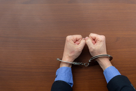 Top view, handcuffed hands of an arrested criminal on the table of the police station. copy spaceの写真素材