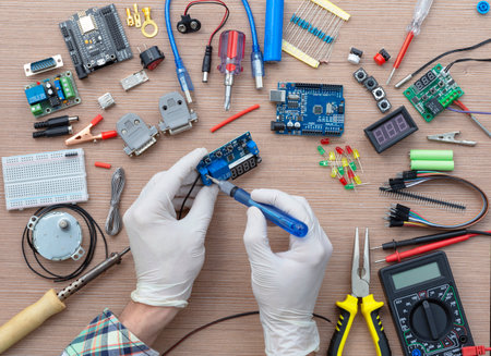 An engineer's hands are assembling a breadboard from an Arduino microcontroller, surrounded by electronics tuning tools. View of the electronic laboratory bench with peripherals and expansion boards.の写真素材