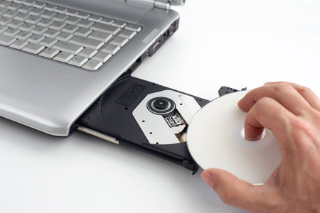 hand inserts dvd disc into laptop, concept of burning data to dvd on isolating backgroundの写真素材