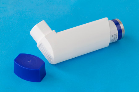 Asthma inhaler with blank label isolated on a blue background. Pharmaceutical product is used to...