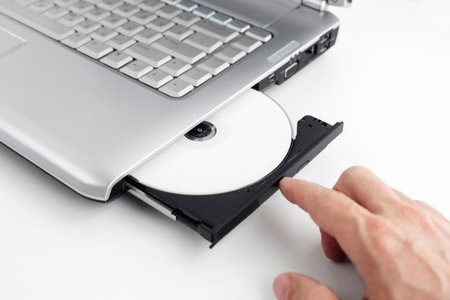 hand inserts dvd disc into laptop, concept of burning data to dvd on isolating background