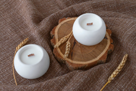 aromatic candles with wooden wick in plaster candlestick, close-up on burlap background, handmade conceptの写真素材