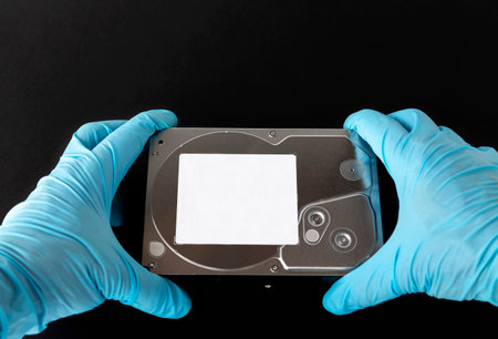 A gloved hand passes a hard drive, a simple hard drive, close-up isolated on a black background,...