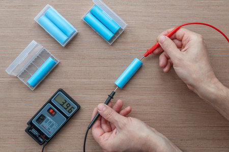 Top view of a technician's hands using a multimeter to test voltage on 18650 lithium-ion battery cells.の写真素材