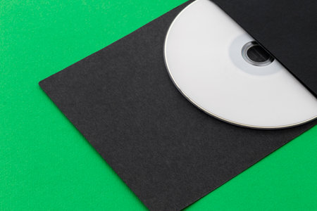 White CD, DVD, Blu Ray, Optical Disc printed side up in black envelope, on green backgroundの写真素材