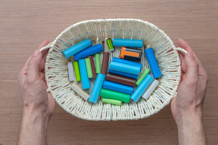Top view, male hands holding a basket with batteries of different sizes for electrical appliances above the table.の写真素材