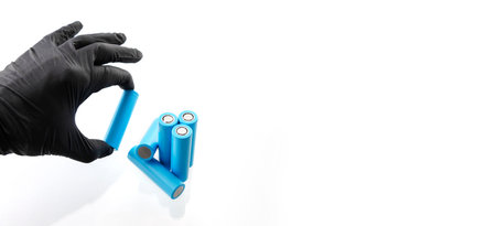 Hand in glove holds light blue rechargeable lithium-ion battery type 18650 for electrical appliances and devices, on isolated background, with space for text.の写真素材