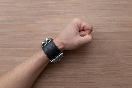 Close-up of a man's hand with a leather bracelet, punching the table. Accessories for rockers, bikers, metalheads, goths and punks. Steampunk style. View from above, with space for text.の写真素材