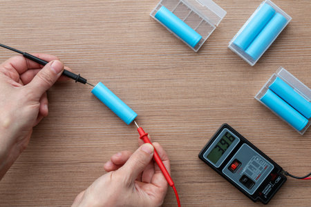 Top view of a technician's hands using a multimeter to test voltage on 18650 lithium-ion battery cells.の写真素材