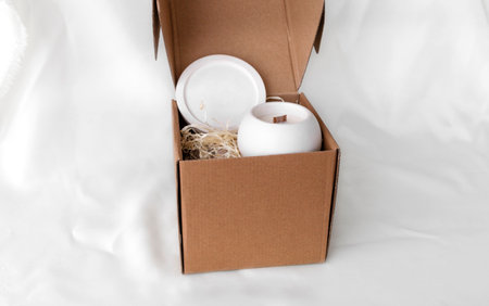 handmade scented candles in cardboard gift box on crumpled white fabric, space for text, gift conceptの写真素材