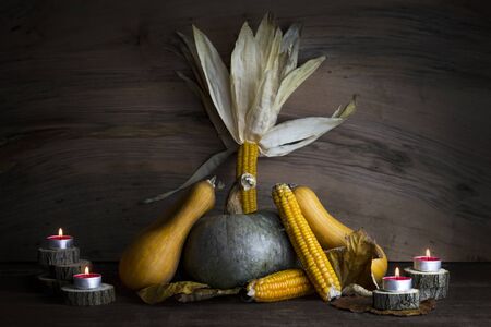 Pumpkin, Corncob, autumn leaves and burning candles Decoration on a wooden tableの写真素材