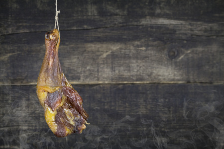 Smoked Chicken Leg Hanging on the Rope Against Wooden Background With Smokeの写真素材