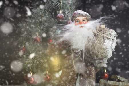 Santa Claus Outdoors Beside Christmas Tree in Snowfall Carrying Gifts to Children. Merry Christmas & New Year's Eve conceptの写真素材