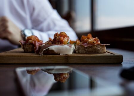 Spanish Tapas Served in Restaurant on Rustic Wooden Board. Bruschetta with Prosciutto, Tomatoes, Ruccola and Spices
の写真素材