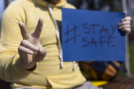 Stay safe sign on blue chroma key paper held by a man in surgical gloves giving victory sign with handの写真素材