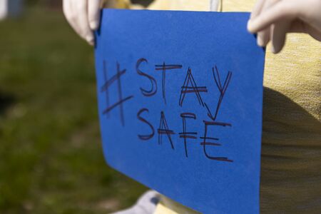 Stay safe sign on blue chroma key paper held by a man in surgical gloves