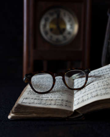 Old worn Glasses resting on an opened book with books and clock in background. Reading time conceptの写真素材