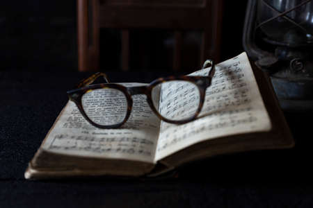 Old worn Glasses resting on an opened book with books and clock in background. Reading time conceptの写真素材