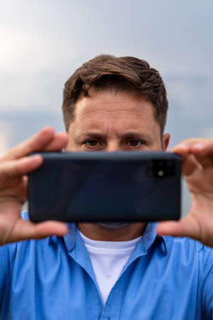 Man holding smartphone in his hands at river and taking photographsの写真素材