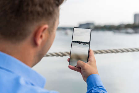Man holding smartphone in his hand beside the river and making photographsの写真素材