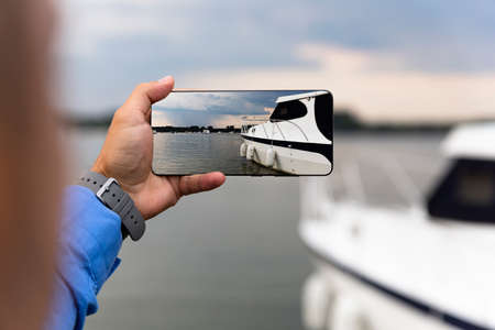 Man photographing Yacht with smartphone at the riverの写真素材