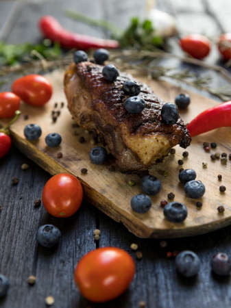 Goose breast Christmas roast with blueberries, tomatoes, red peppers and rosemary served on a wooden boardの写真素材