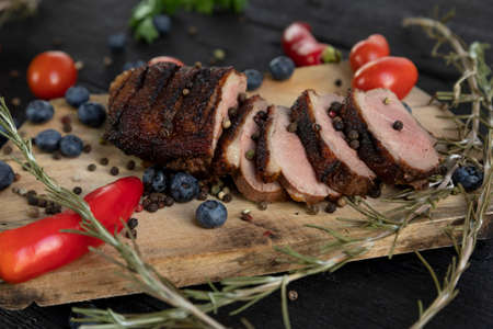 Goose breast Christmas roast with blueberries, tomatoes, red peppers and rosemary served on a wooden boardの写真素材