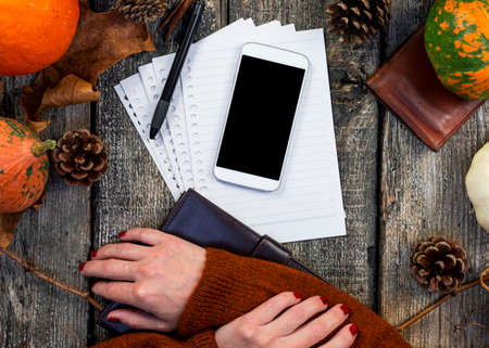 Smartphone with blank screen for copy space and notepad on wooden table with pumpkins, fall colorful leaves, autumn composition, Thanksgiving, concept. Top view.の写真素材
