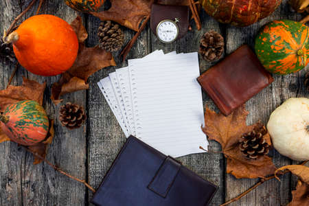 Blank notepad on a rustic wooden table with pumpkins, autumn leaves, pocket watch and leather wallet. Fall and Thanksgiving concept. For Copy spaceの写真素材