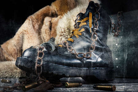 Leather boot with rusted chains and bullet shells with military gas mask and fur coat in background...