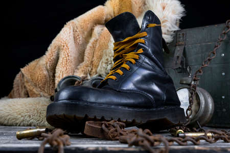 Leather boot with rusted chains and bullet shells with military gas mask and fur coat in background...