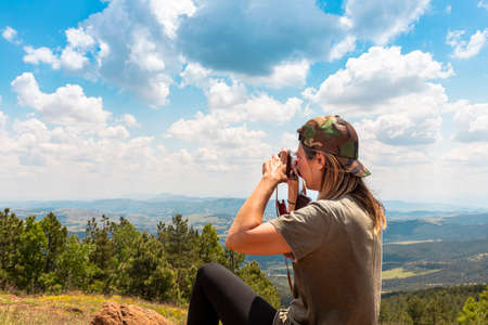 Tourist girl photographing with vintage photo camera at the top of the mountain peakの写真素材