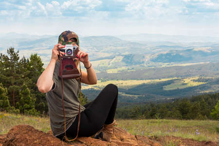 Tourist girl photographing with vintage photo camera at the top of the mountain peakの写真素材