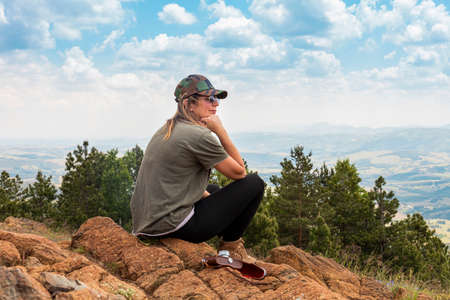 Tourist girl hiker, photographer resting at the top of the mountain and enjoying amazing landscape view of mountains and beautiful skyの写真素材