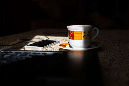 Coffe cup on the table with smartphone and lap top. Selective focus on the mugの写真素材