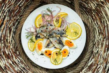 Herring fish fillets with eggs, herbs, onion and lemon on a white plate in the kitchen. Top view, flat lay photoの写真素材