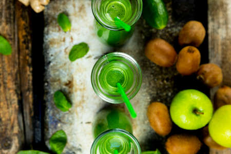 Healthy green smoothies with spinach, apple, kiwi, broccoli and mint in glass jar with fruits and...