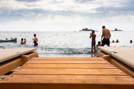 Empty wooden table at the beach with people swimming at sea in background. Empty, blank space for...
