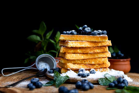 Waffles with fresh blueberries and powdered sugar on the rustic table. Freshly baked Belgian waffles