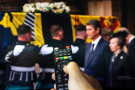 Belgrade, Serbia - September 12, 2022: Queen Elizabeth II coffin carried in to the Palace of Holyroodhouse, Scotland. Watching news on tv about late Queen of United Kingdom with remote controle in hand. Remembering and honoring her Majesty Queen Elizabethのeditorial素材
