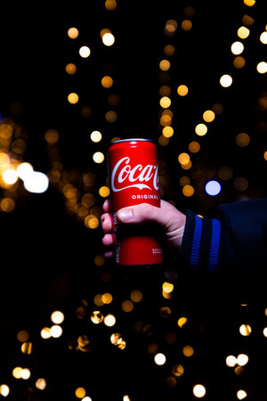 Belgrade, Serbia - January 5, 2023: Coca Cola can in hand with Christmas lights and decoration in...