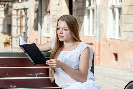 girl with pink bicycle and grocery basket sitting on street bench and reading bookの写真素材