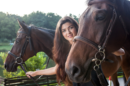 Pretty young woman walking two horses outdoorの写真素材