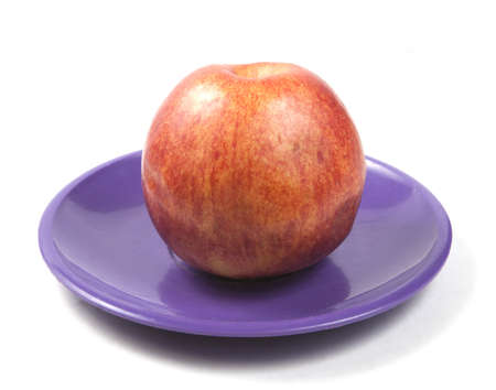Red apple lying on a purple plastic dishの写真素材